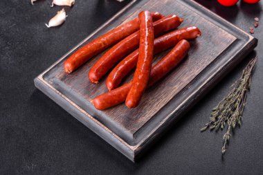 Lezzetli taze füme sıcak sosis, kiraz domatesli ve domates soslu koyu beton bir masada.