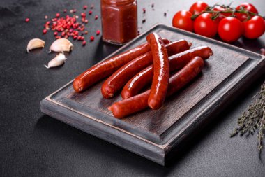 Lezzetli taze füme sıcak sosis, kiraz domatesli ve domates soslu koyu beton bir masada.