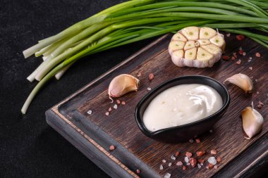 Sarımsak sosu seramik siyah sosta. Koyu beton bir masada ahşap kesme tahtasının üzerinde yeşillik var.