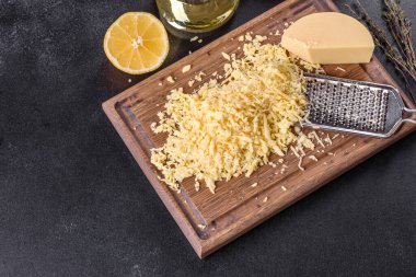 Koyu beton arka planda tahta kesme tahtasındaki büyük rende rendelenmiş taze sert peynir.