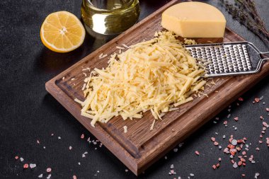 Koyu beton arka planda tahta kesme tahtasındaki büyük rende rendelenmiş taze sert peynir.