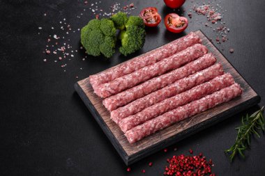 Koyu beton bir masanın üzerindeki tahta kesme tahtasına baharatlı taze çiğ domuz sosisi.