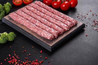 Koyu beton bir masanın üzerindeki tahta kesme tahtasına baharatlı taze çiğ domuz sosisi.