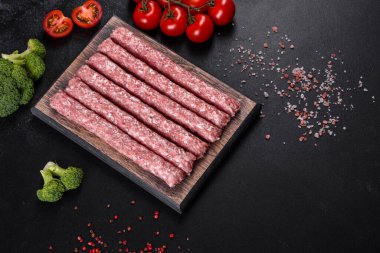Koyu beton bir masanın üzerindeki tahta kesme tahtasına baharatlı taze çiğ domuz sosisi.