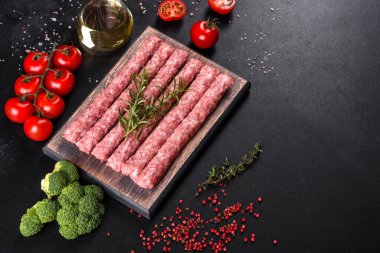 Koyu beton bir masanın üzerindeki tahta kesme tahtasına baharatlı taze çiğ domuz sosisi.