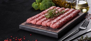 Koyu beton bir masanın üzerindeki tahta kesme tahtasına baharatlı taze çiğ domuz sosisi.