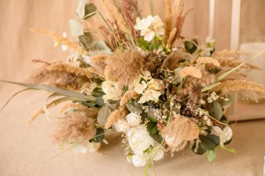 Beyaz bir vazoda, bej kumaş arkaplanda duran kuru ve güzel çiçeklerin süslemeleri. Ev dekorasyonu