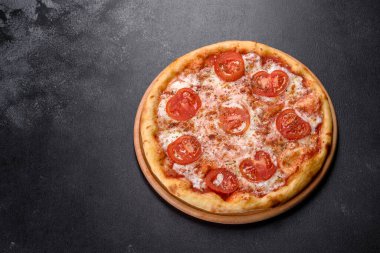 Lezzetli fırında pizza, domatesli ve peynirli koyu beton arka planda.