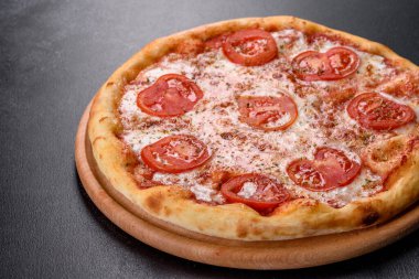 Lezzetli fırında pizza, domatesli ve peynirli koyu beton arka planda.