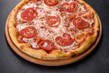 Lezzetli fırında pizza, domatesli ve peynirli koyu beton arka planda.