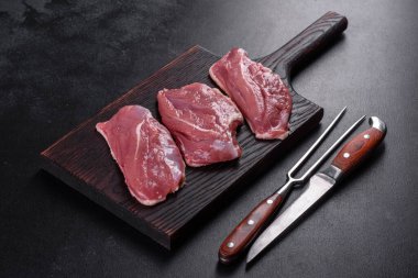 Çiğ ördek göğsü, otlar ve baharatlarla koyu beton bir arka planda. Pişirmeye hazır çiğ et.