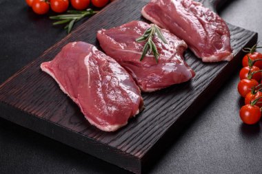 Çiğ ördek göğsü, otlar ve baharatlarla koyu beton bir arka planda. Pişirmeye hazır çiğ et.