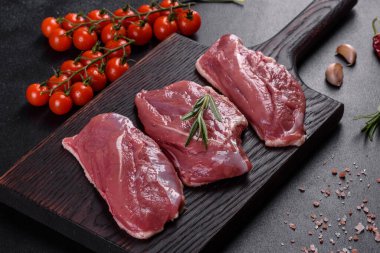 Çiğ ördek göğsü, otlar ve baharatlarla koyu beton bir arka planda. Pişirmeye hazır çiğ et.