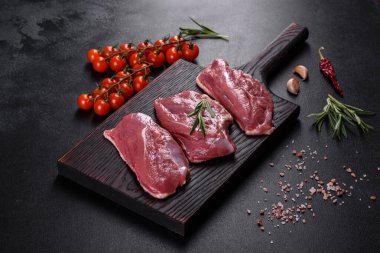 Çiğ ördek göğsü, otlar ve baharatlarla koyu beton bir arka planda. Pişirmeye hazır çiğ et.