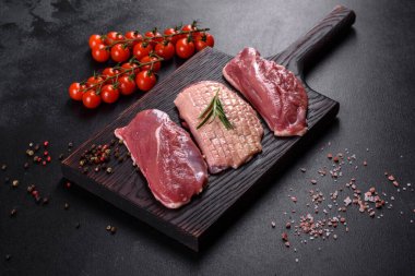 Çiğ ördek göğsü, otlar ve baharatlarla koyu beton bir arka planda. Pişirmeye hazır çiğ et.