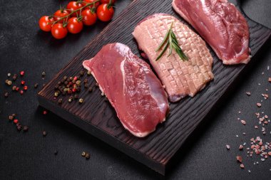 Çiğ ördek göğsü, otlar ve baharatlarla koyu beton bir arka planda. Pişirmeye hazır çiğ et.