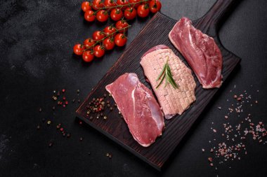 Çiğ ördek göğsü, otlar ve baharatlarla koyu beton bir arka planda. Pişirmeye hazır çiğ et.