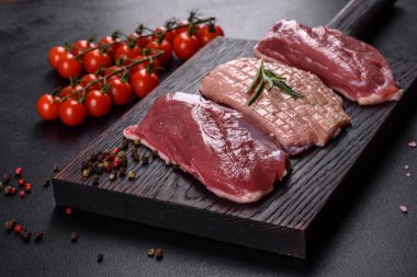 Çiğ ördek göğsü, otlar ve baharatlarla koyu beton bir arka planda. Pişirmeye hazır çiğ et.