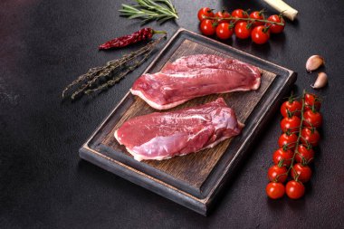 Çiğ ördek göğsü, otlar ve baharatlarla koyu beton bir arka planda. Pişirmeye hazır çiğ et.