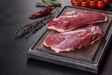 Çiğ ördek göğsü, otlar ve baharatlarla koyu beton bir arka planda. Pişirmeye hazır çiğ et.