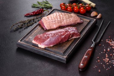 Çiğ ördek göğsü, otlar ve baharatlarla koyu beton bir arka planda. Pişirmeye hazır çiğ et.