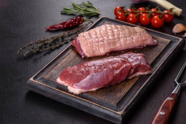 Çiğ ördek göğsü, otlar ve baharatlarla koyu beton bir arka planda. Pişirmeye hazır çiğ et.