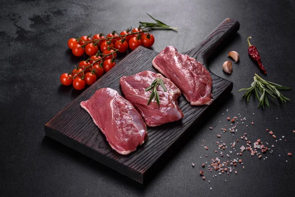 Çiğ ördek göğsü, otlar ve baharatlarla koyu beton bir arka planda. Pişirmeye hazır çiğ et.