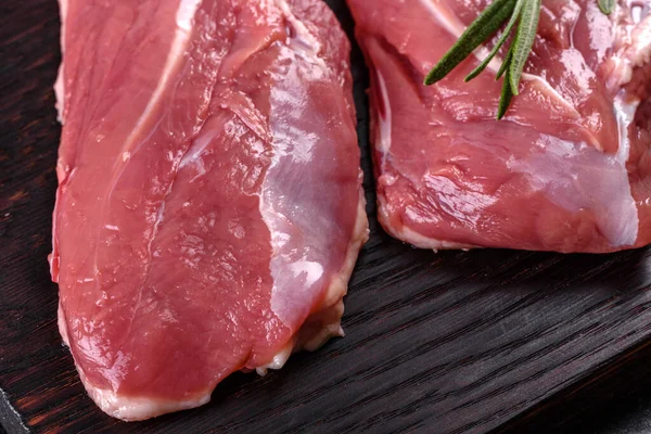 Çiğ ördek göğsü, otlar ve baharatlarla koyu beton bir arka planda. Pişirmeye hazır çiğ et.