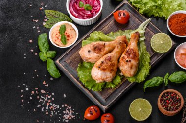 Lezzetli ızgara tavuk budu, ahşap bir tahta üzerinde baharat ve otlar, koyu beton bir arka plan. Yemek ateşte pişiyor.