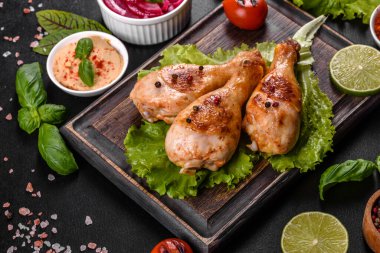 Lezzetli ızgara tavuk budu, ahşap bir tahta üzerinde baharat ve otlar, koyu beton bir arka plan. Yemek ateşte pişiyor.