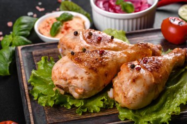 Lezzetli ızgara tavuk budu, ahşap bir tahta üzerinde baharat ve otlar, koyu beton bir arka plan. Yemek ateşte pişiyor.