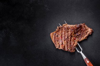 Delicious juicy fresh beef steak with spices and herbs on a dark concrete background. Grilled dishes clipart