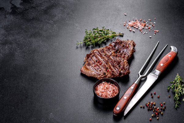 Delicious juicy fresh beef steak with spices and herbs on a dark concrete background. Grilled dishes