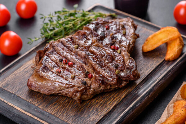 Delicious juicy fresh beef steak with spices and herbs on a dark concrete background. Grilled dishes