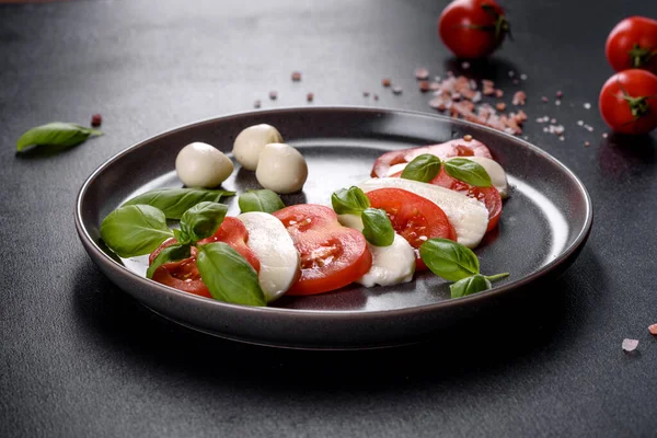スライスしたトマトとイタリアのカプレーゼサラダ モッツァレラチーズ バジル オリーブオイル ダークコンクリートの背景にヴィンテージブラックプレートで提供 — ストック写真