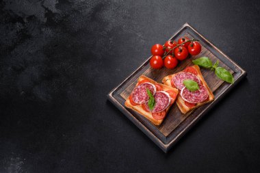 Koyu beton arka planda kurutulmuş İspanyol sosisi salamı. Lezzetli taze sandviçlerin hazırlığı