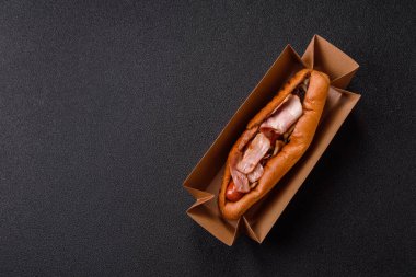 A hot dog with sausage, bacon, sauces, and a bun, unhealthy takeaway food. A hot dog with bacon as a food background for your design.