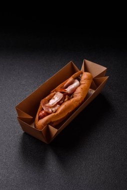 A hot dog with sausage, bacon, sauces, and a bun, unhealthy takeaway food. A hot dog with bacon as a food background for your design.