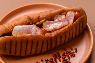 A hot dog with sausage, bacon, sauces, and a bun, unhealthy takeaway food. A hot dog with bacon as a food background for your design.