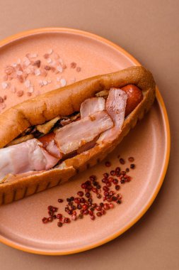 A hot dog with sausage, bacon, sauces, and a bun, unhealthy takeaway food. A hot dog with bacon as a food background for your design.