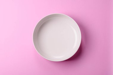 Mutfak malzemesi olarak pembe arka planda boş bir seramik tabak. Tasarımınız için yiyecek arka planı olarak boş bir tabak