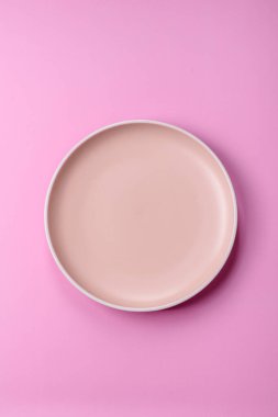Mutfak malzemesi olarak pembe arka planda boş bir seramik tabak. Tasarımınız için yiyecek arka planı olarak boş bir tabak