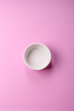 Mutfak malzemesi olarak pembe arka planda boş bir seramik tabak. Tasarımınız için yiyecek arka planı olarak boş bir tabak