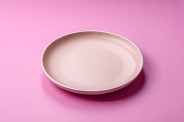 Mutfak malzemesi olarak pembe arka planda boş bir seramik tabak. Tasarımınız için yiyecek arka planı olarak boş bir tabak