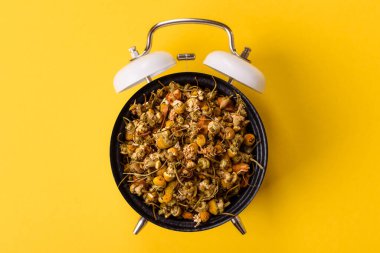 Kurumuş papatya çiçekleri, sıcak bir sabah içeceği için kâsede bitki çayı. Eski bir çalar saatin kadranı yerine tabak konsepti olarak kurutulmuş papatya çayı.