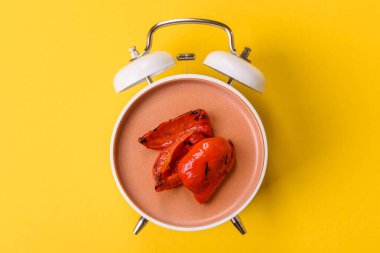 Izgara kırmızı biber, vejetaryen yemeği. Kırmızı çan biberleri eski bir çalar saatin kadranı yerine tabak konsepti olarak kullanılıyor.