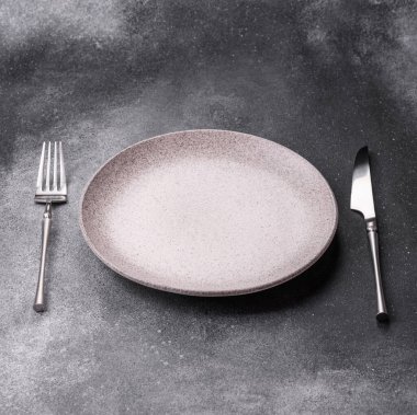 Boş bir seramik tabak, bıçak ve çatal yemek masası olarak kullanılıyor. Tasarımınız için arka plan olarak boş bir tabak