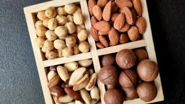 Sağlıklı beslenmek için macadamia fındığı, badem, şam fıstığı ve fındık içeren ahşap kutu. Tasarımınız için yemek arkaplanı olarak fındık