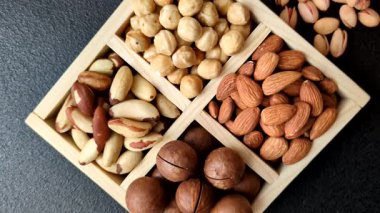 Sağlıklı beslenmek için macadamia fındığı, badem, şam fıstığı ve fındık içeren ahşap kutu. Tasarımınız için yemek arkaplanı olarak fındık