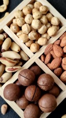 Sağlıklı beslenmek için macadamia fındığı, badem, şam fıstığı ve fındık içeren ahşap kutu. Tasarımınız için yemek arkaplanı olarak fındık